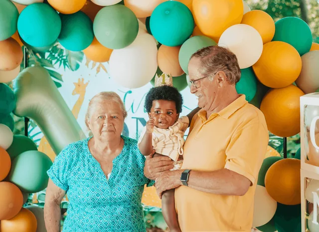Grandparents hold the birthday boy together in front of the balloon wall