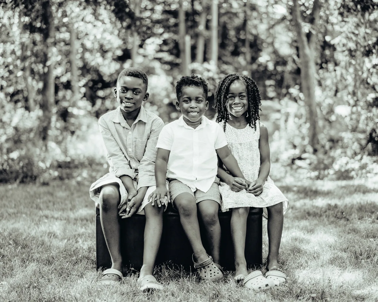 Three children sit side by side on a bench in a backyard