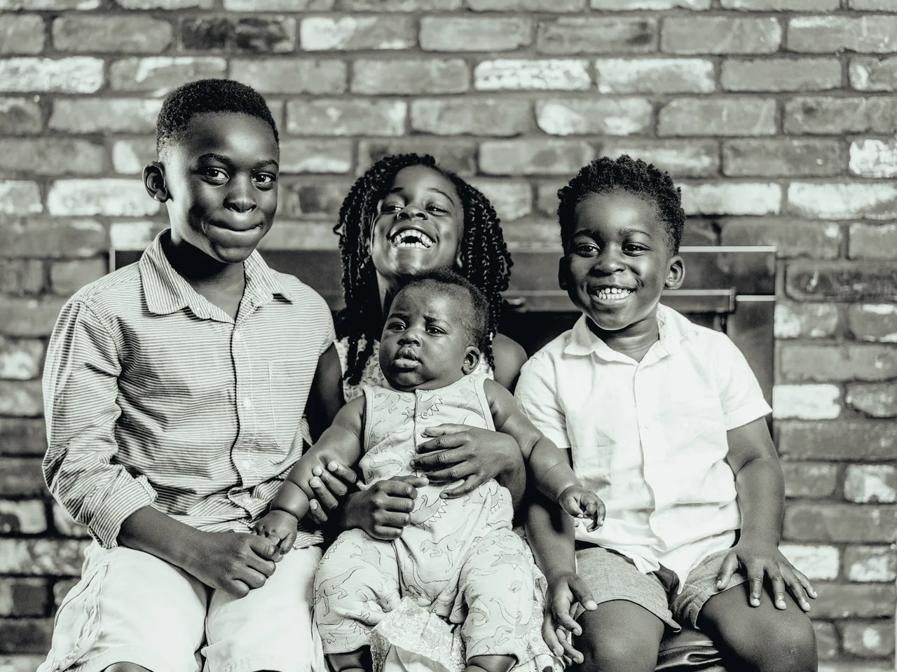 Four siblings laugh together on a bench in front of a brick wall