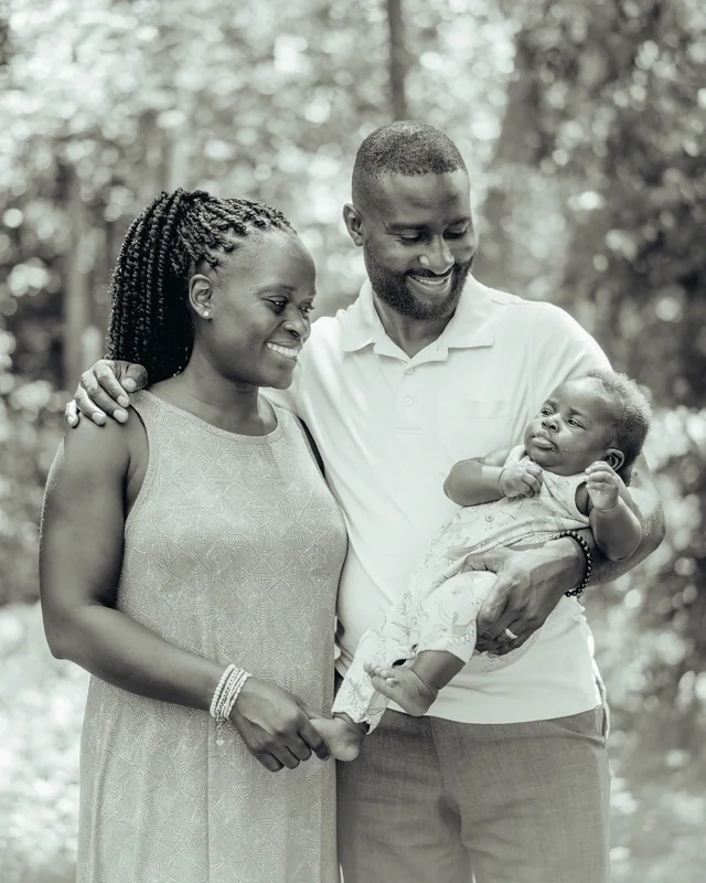 A mother and father stand close together, the father holding their baby