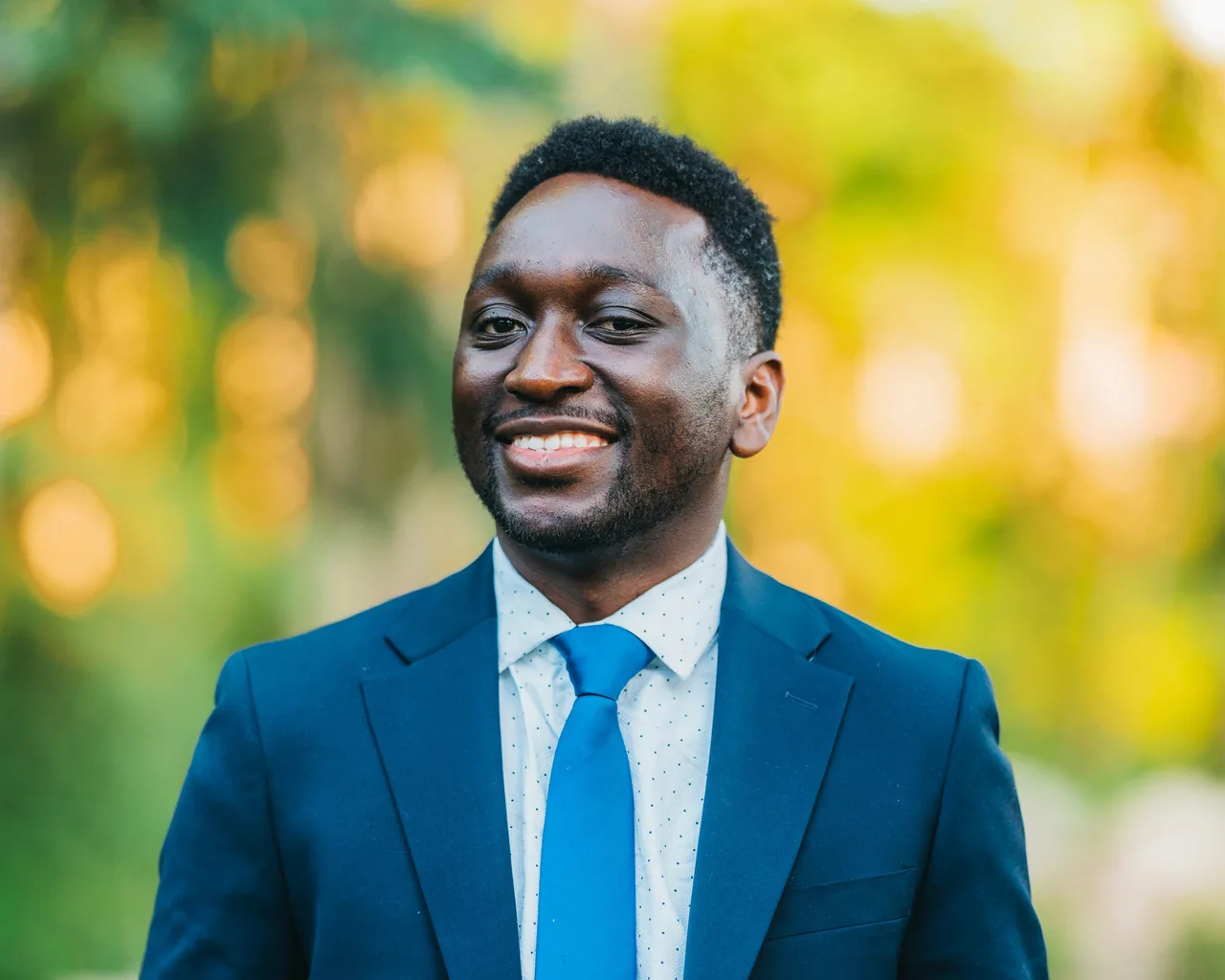 Close portrait of a smiling man wearing a blue suit and tie outdoors