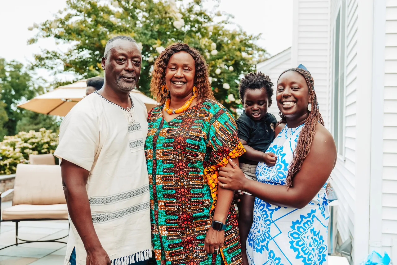Four people, including a small child being held, stand together outdoors in colorful celebration clothing