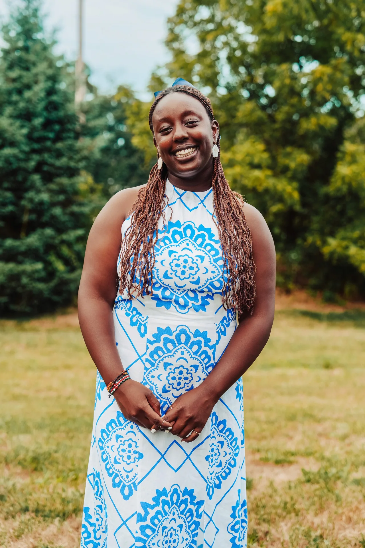 A smiling woman in a blue-and-white patterned dress stands outdoors