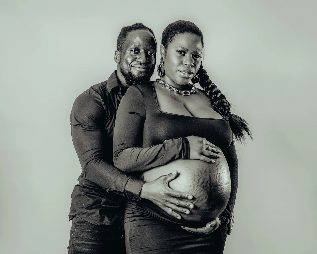 An expecting parent and her partner stand together, their hands resting on her bump