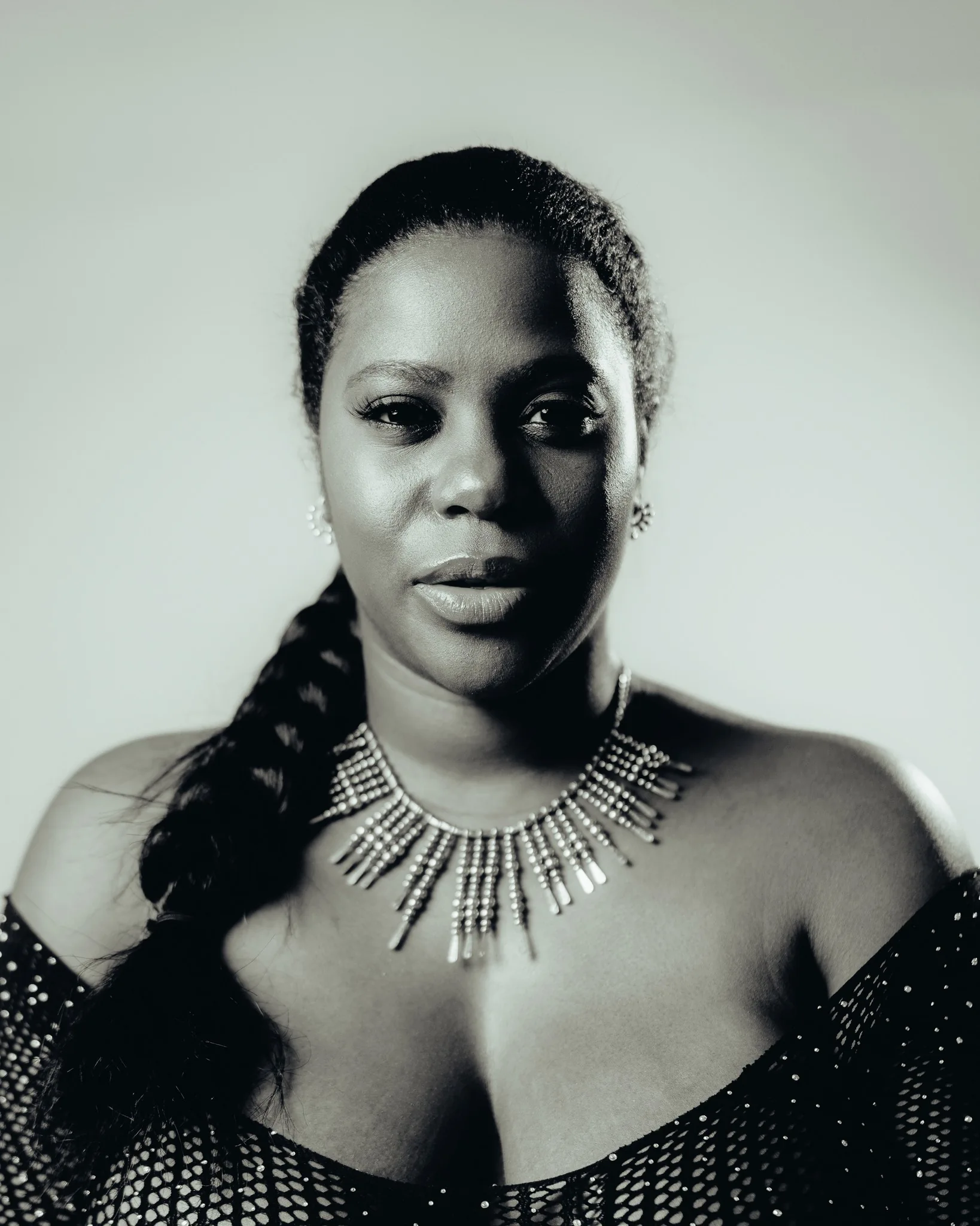 Black-and-white close portrait of a woman wearing a statement necklace against a pale background