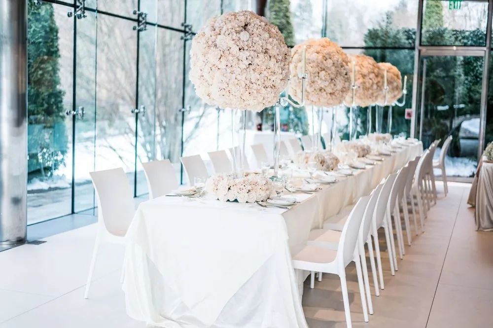 A long reception table with tall blush rose centerpieces set against snowy windows