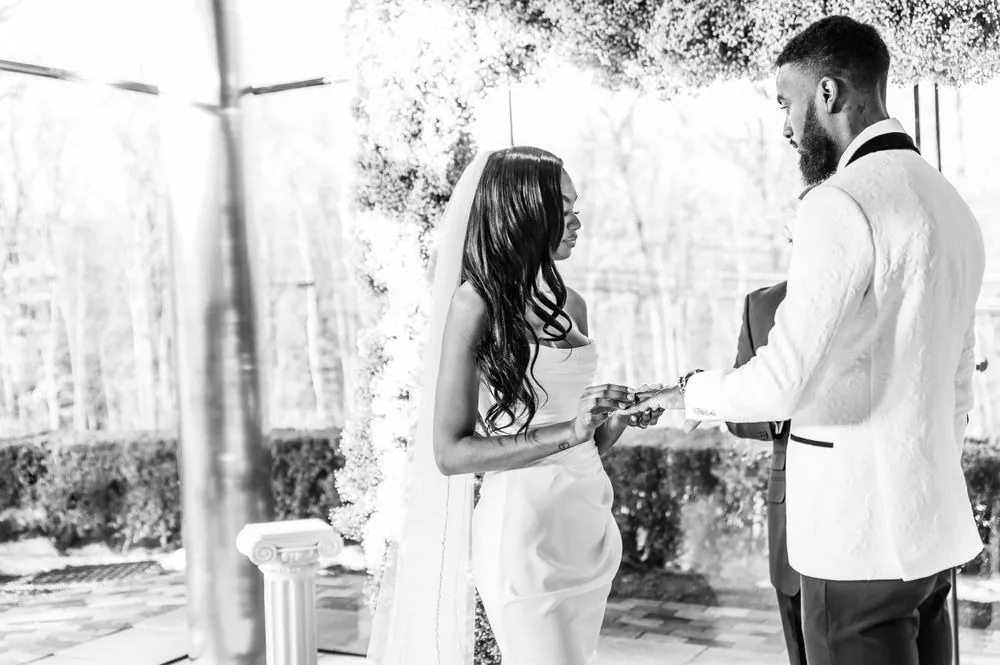 Dontre slides the ring onto Abigail's finger beneath the arch, in black and white
