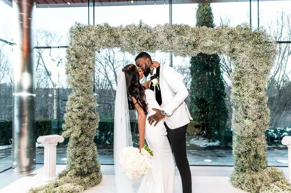 Abigail and Dontre kiss beneath the baby's breath arch as her veil drifts