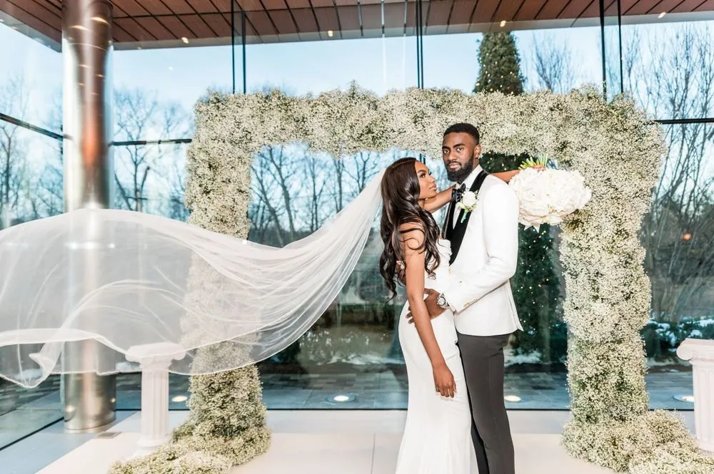 Abigail and Dontre pose under the baby's breath arch as her long veil floats through the air