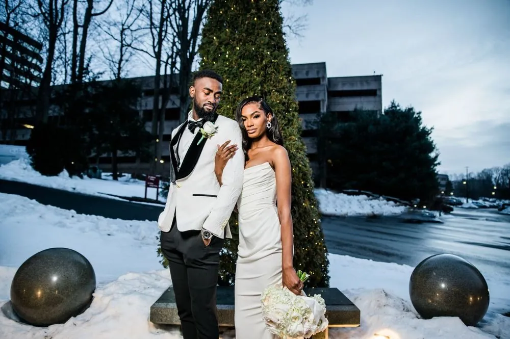 Abigail and Dontre stand before a lit evergreen with snowbanks all around them