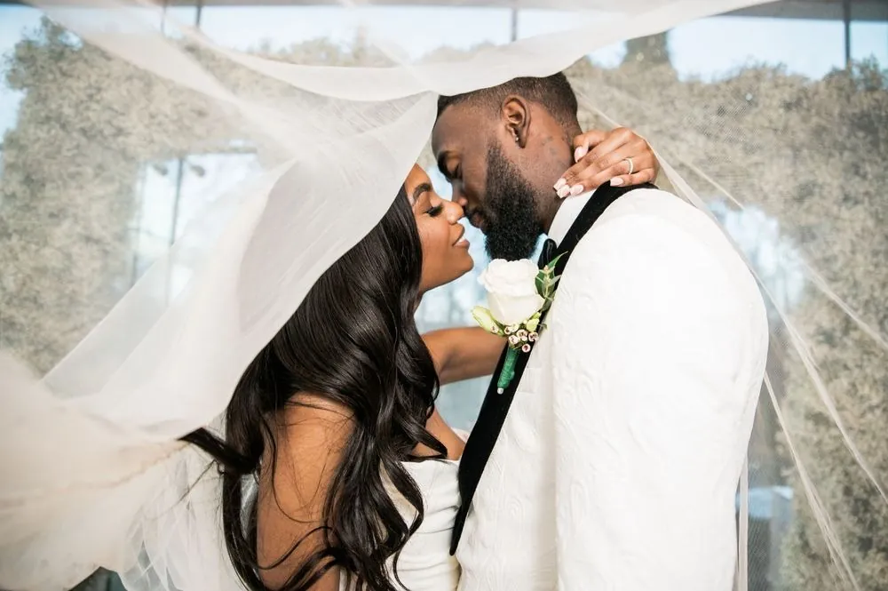 Abigail and Dontre kiss beneath her veil in soft window light