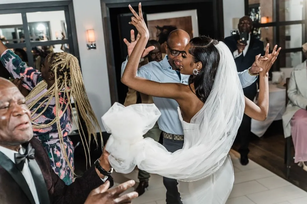 The bride throws her hands up dancing with guests, her veil swinging