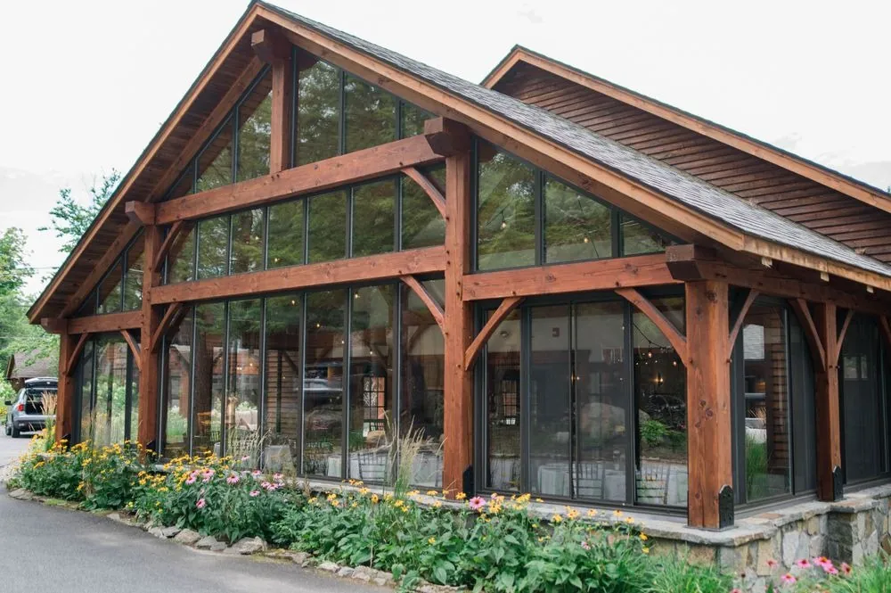 Timber lodge with tall glass windows and a peaked roof on a bright summer day