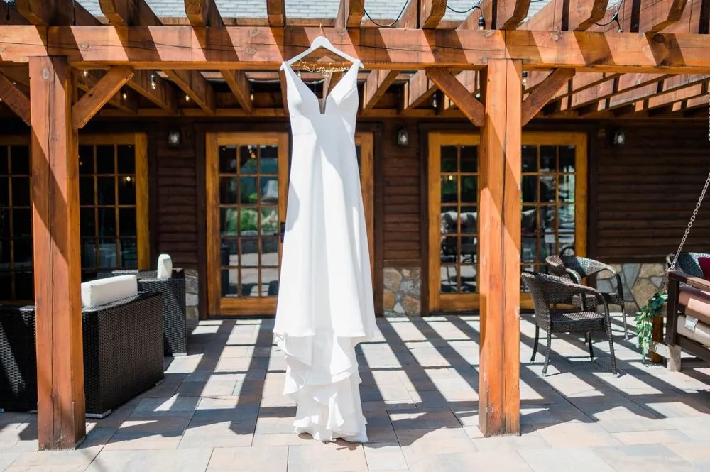 Wedding gown hangs from a beam under a wooden pergola on the stone patio
