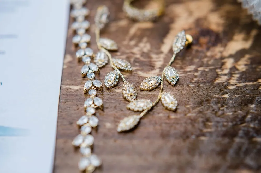 Leaf-shaped bridal earrings and a jeweled hairpiece laid out on wood