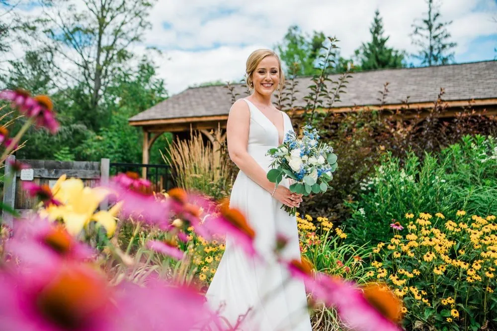 Bride smiles behind a bed of pink coneflowers and yellow blooms near the lodge