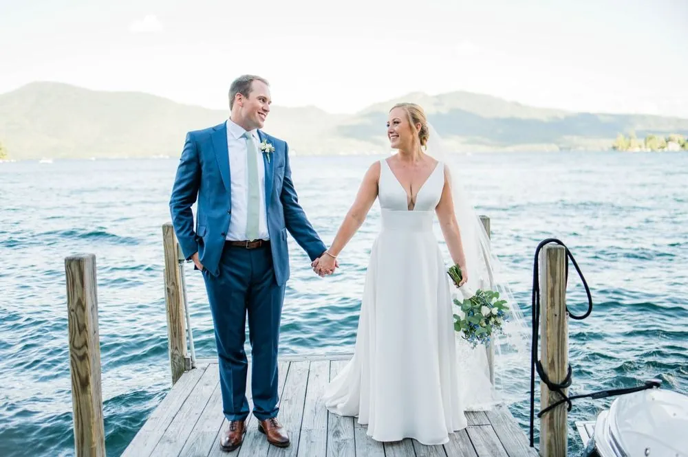 Alexandra and Robert hold hands on a wooden dock over blue lake water and mountains