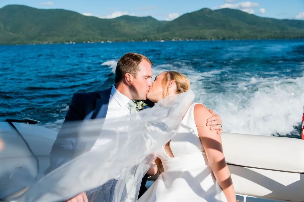 Alexandra and Robert kiss on a speedboat as her veil whips across them over the wake