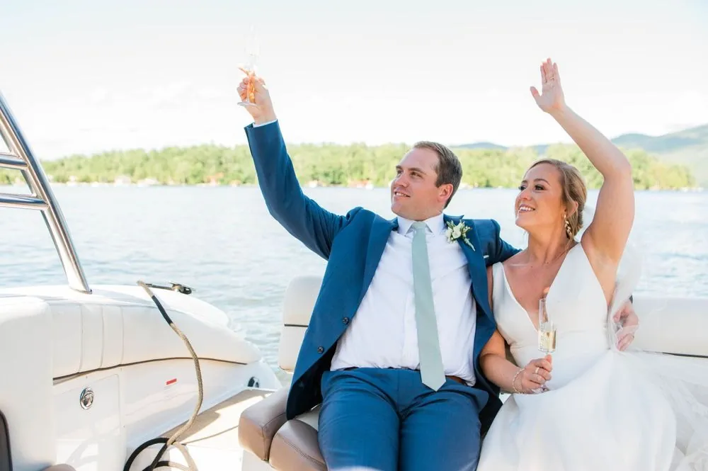 Robert and Alexandra raise champagne and throw their arms up on the boat