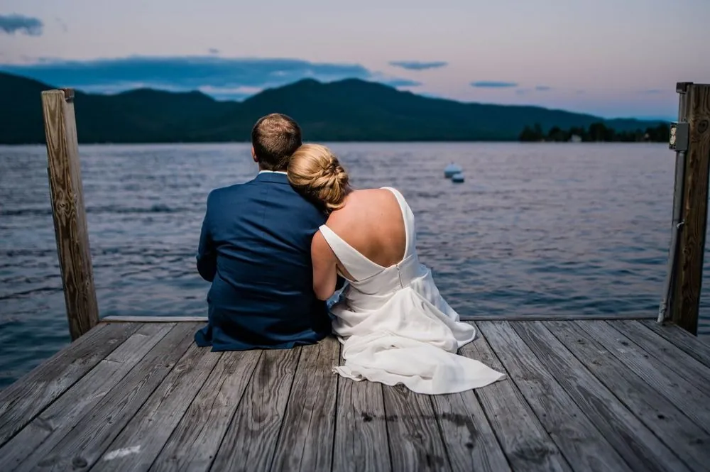 Alexandra rests her head on Robert's shoulder as they sit at the end of the dock at dusk
