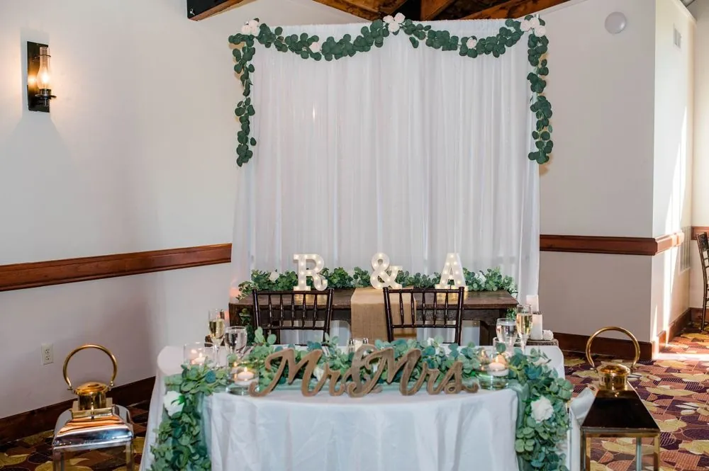 Sweetheart table with eucalyptus garland, R and A marquee letters, and brass lanterns