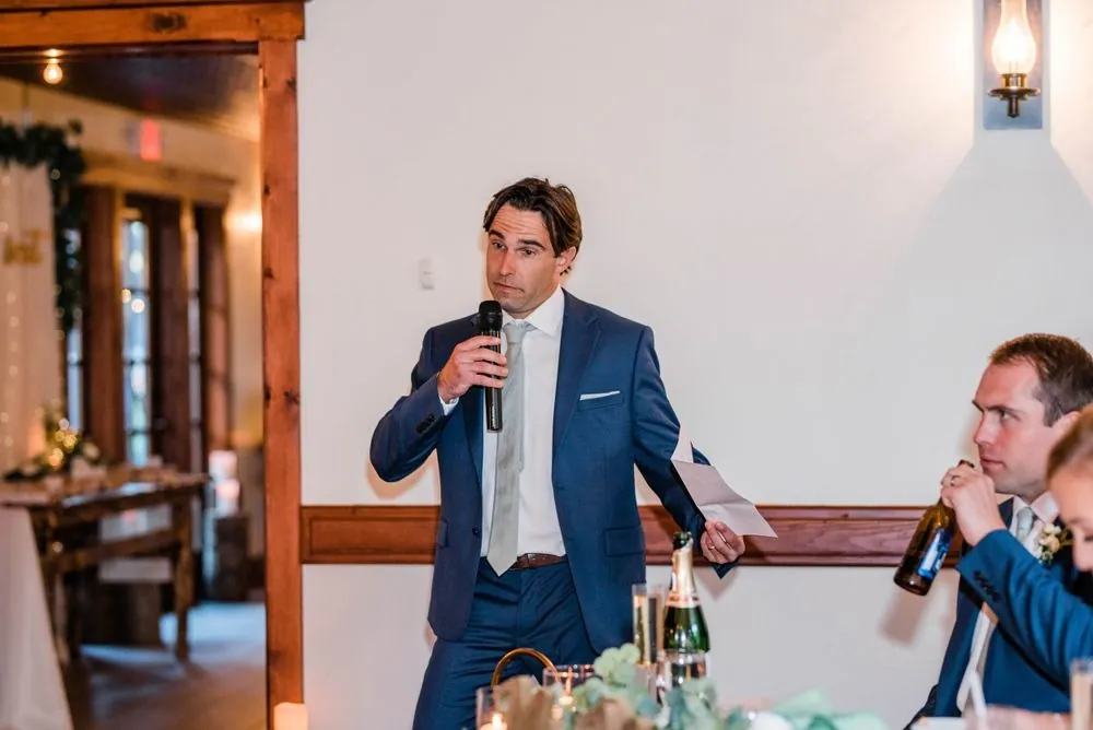 Guest in a navy suit gives a toast into a microphone in the lodge