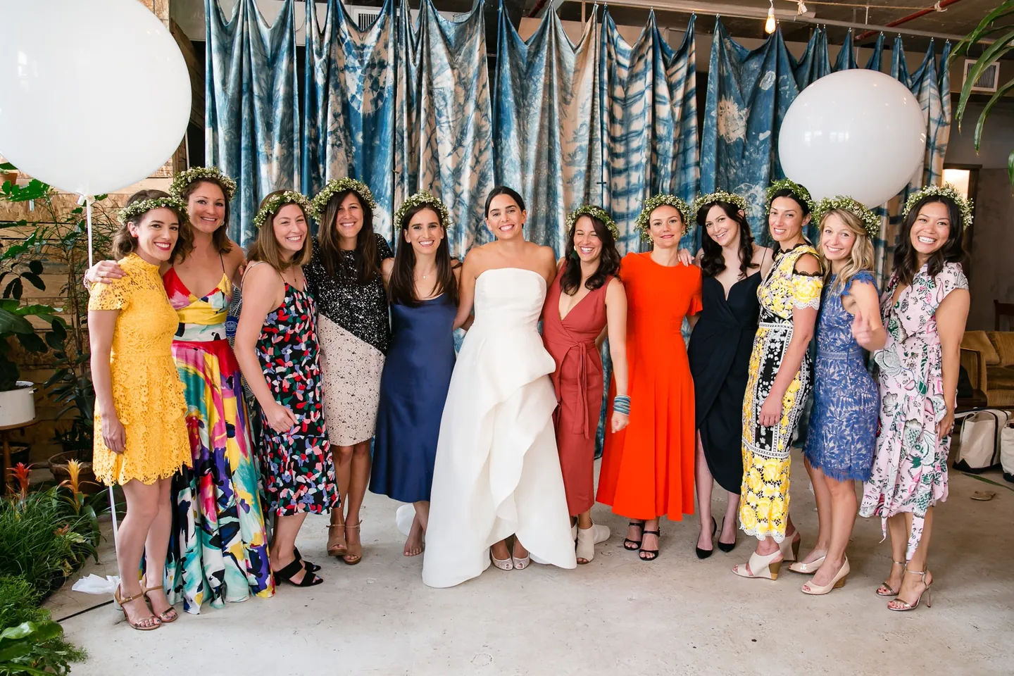 The bride stands with friends in bright summer dresses beneath a floating white balloon