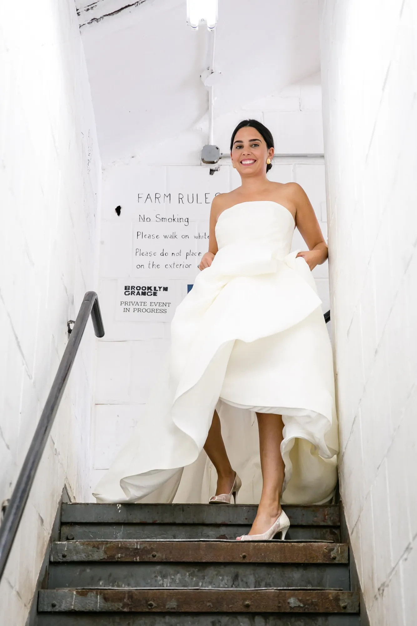 The bride lifts her skirt and descends a narrow white stairwell
