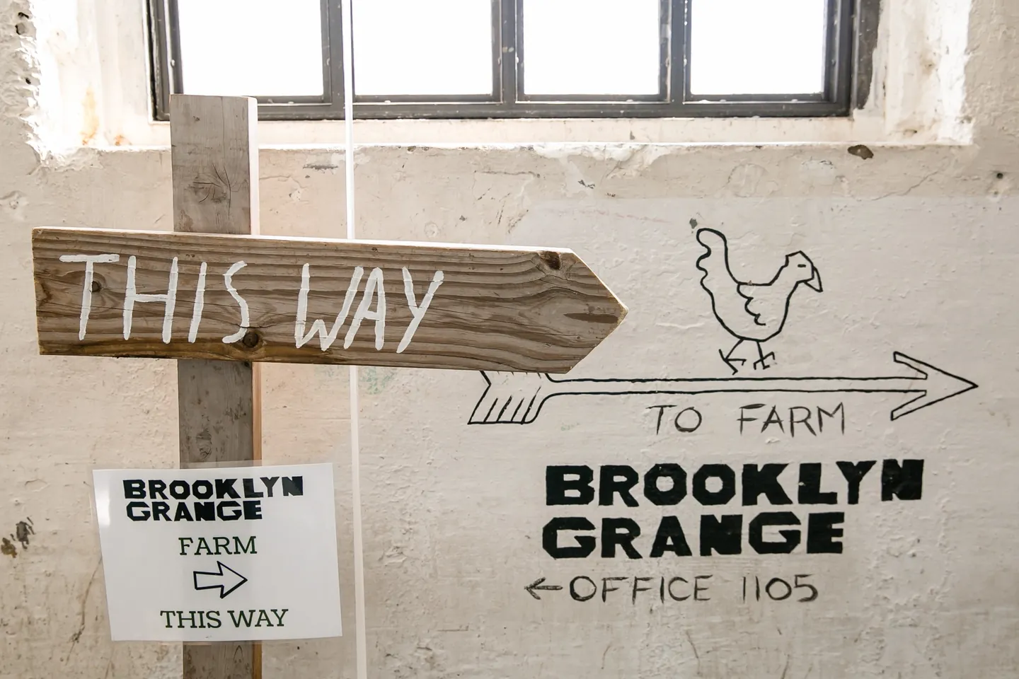 A hand-lettered This Way sign with a chicken arrow pointing toward the rooftop farm