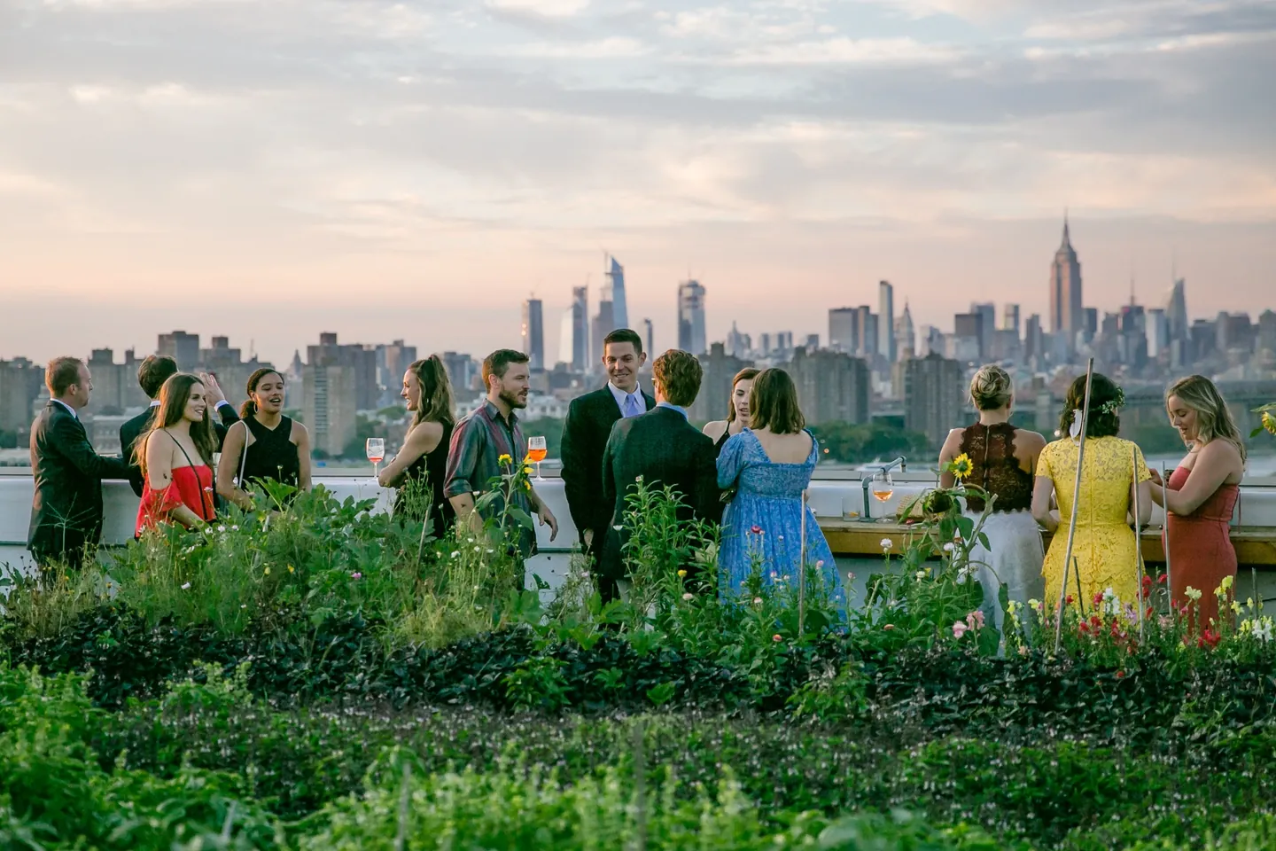 Guests line the roof edge at dusk as the Manhattan skyline turns pink