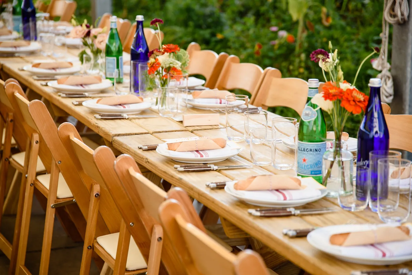 Blue glass bottles, striped napkins, and bread in paper line a long dinner table