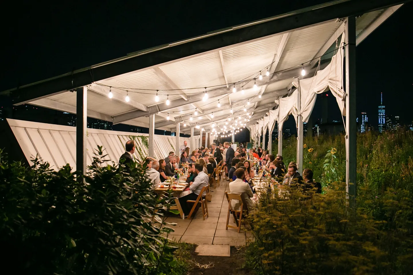 Guests fill the long tables under the lit pergola after dark