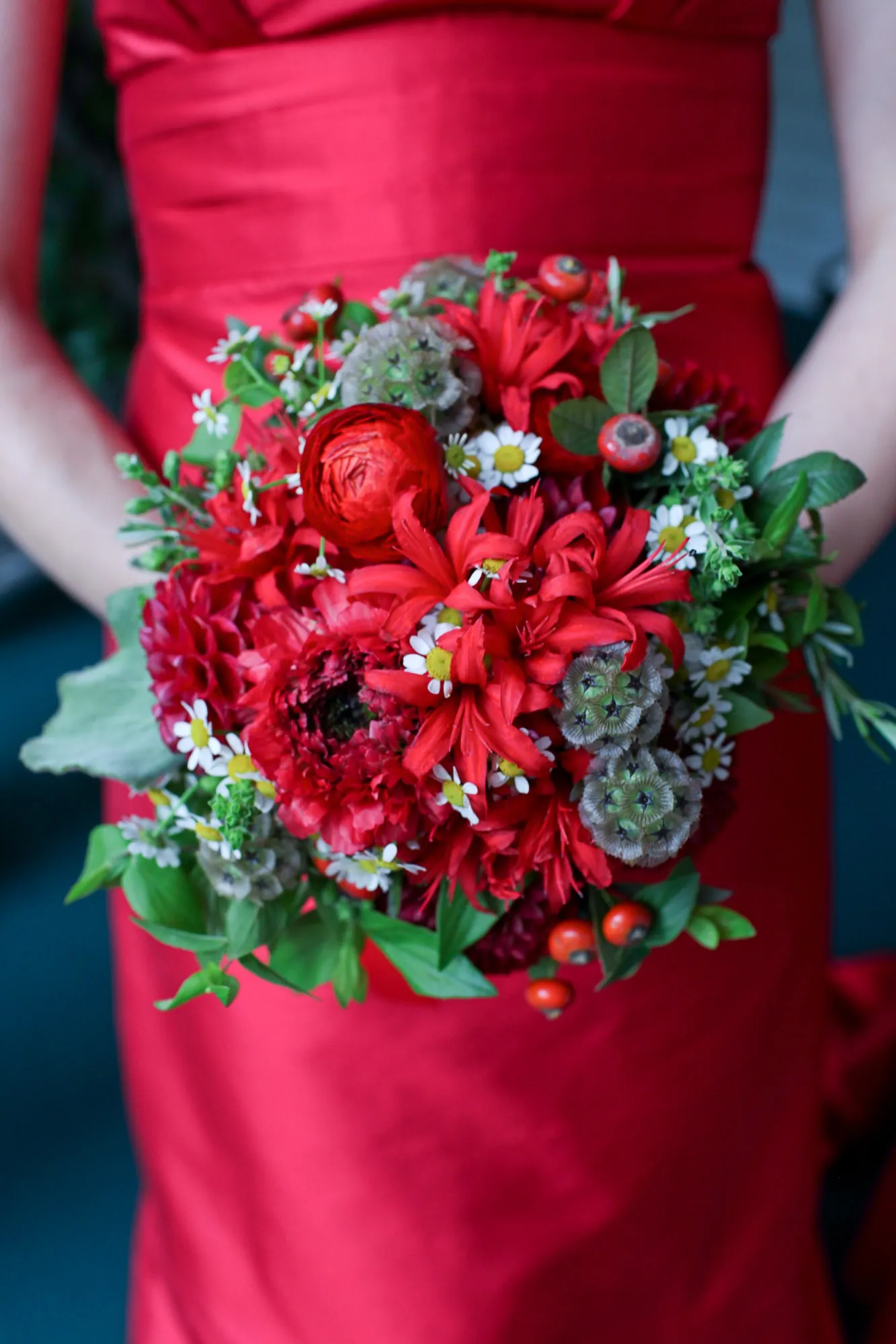 A tight bouquet of red roses and dahlias held against a scarlet gown