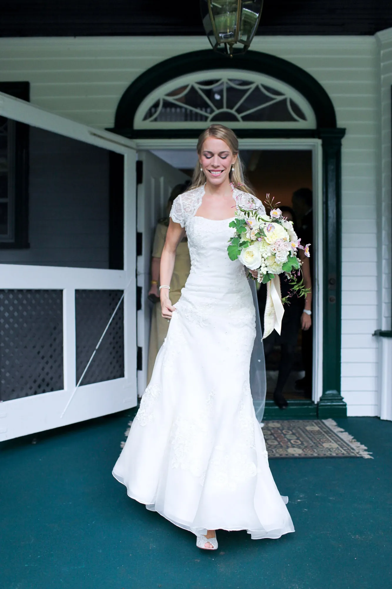 The bride steps through an arched white doorway holding her bouquet