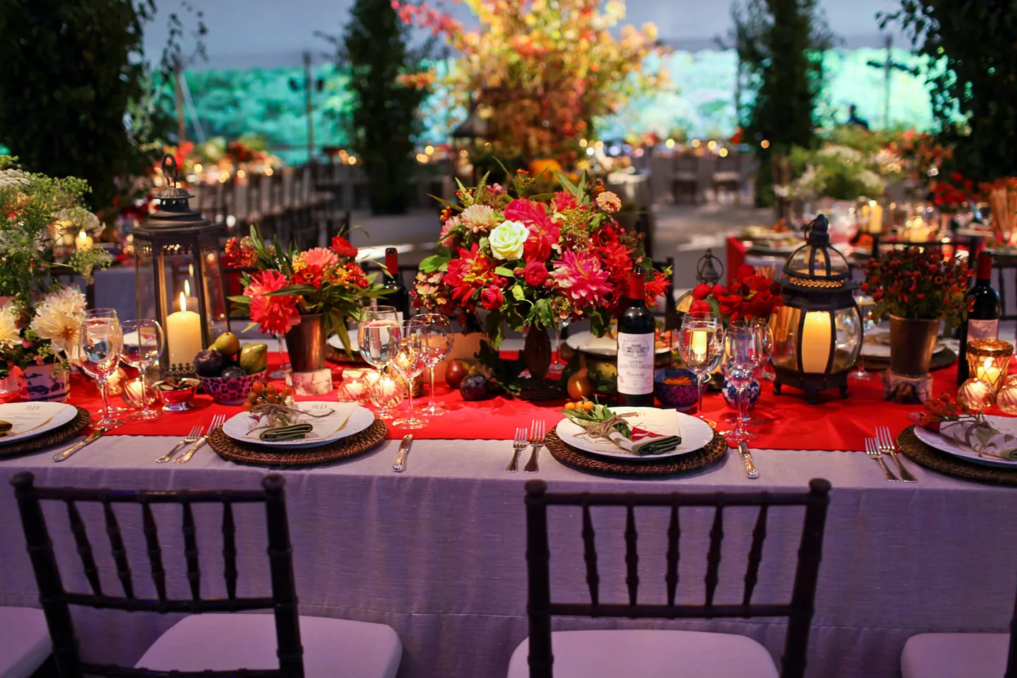 Red and orange flowers and candle lanterns crowd a long table under the tent