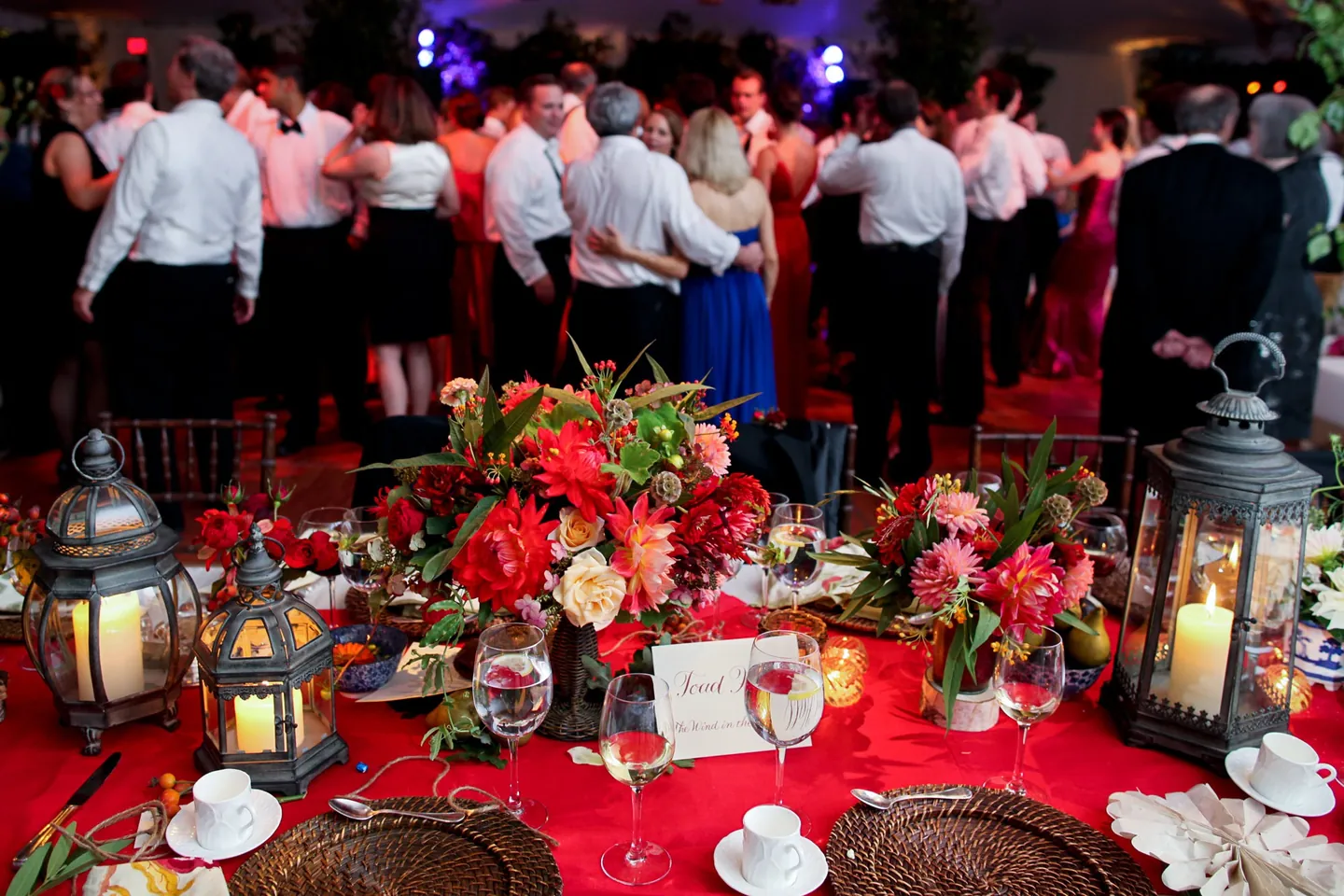Guests fill the dance floor behind a table of lanterns and red flowers