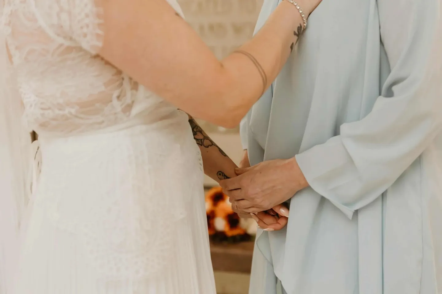 The bride's tattooed hand held between the hands of a woman in pale blue silk