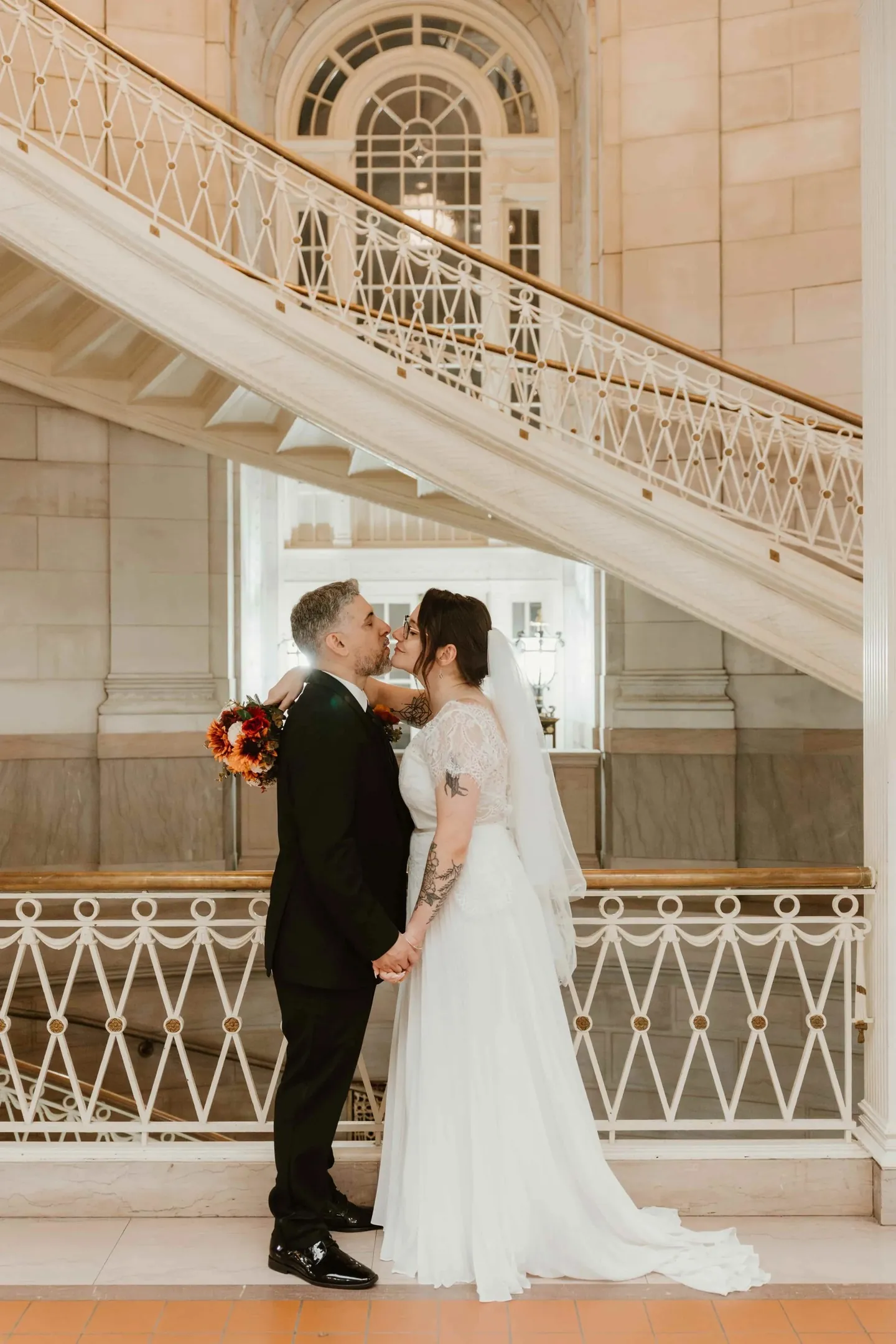 Amber and Marco kiss beside a curving marble staircase with an iron railing