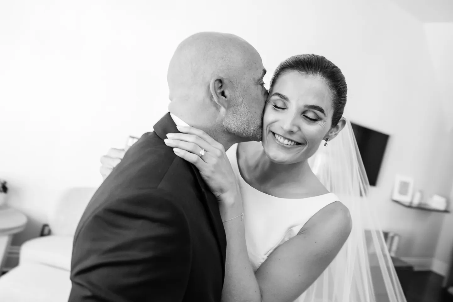 Her father pulls the bride close for a kiss on the cheek, in black and white