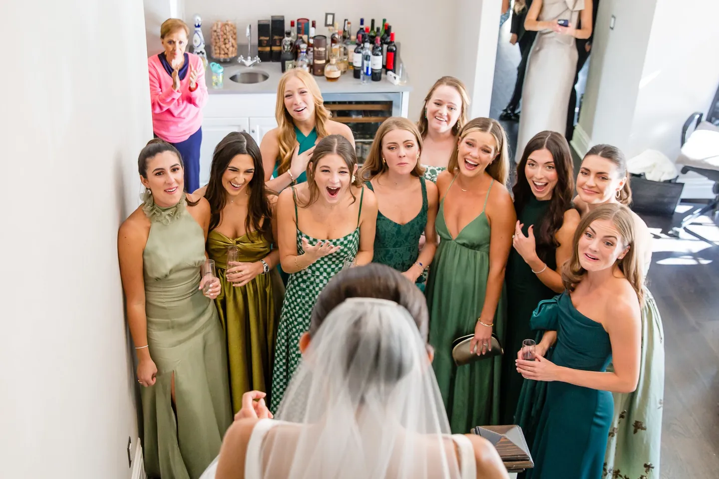 Bridesmaids in green dresses break into wide smiles as the bride turns to face them