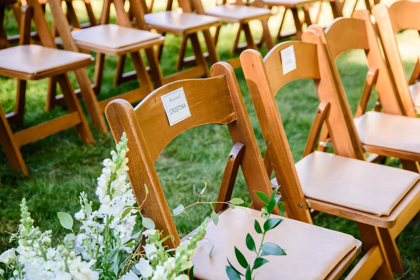 Wooden folding chairs tagged with white flowers line the grassy ceremony aisle