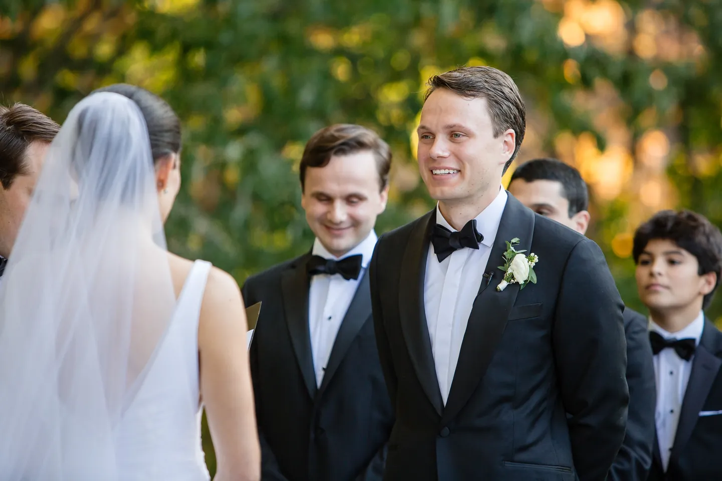 The groom and his groomsmen grin as the bride reaches the front, her veil falling behind her