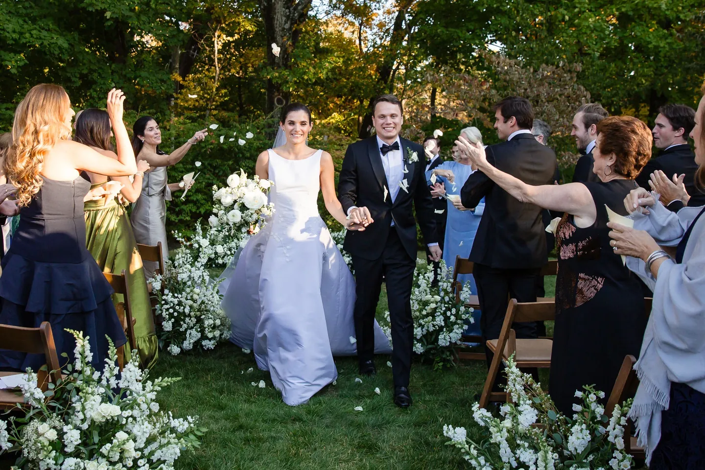 Guests cheer as the newlyweds start back up the aisle between white flower arrangements