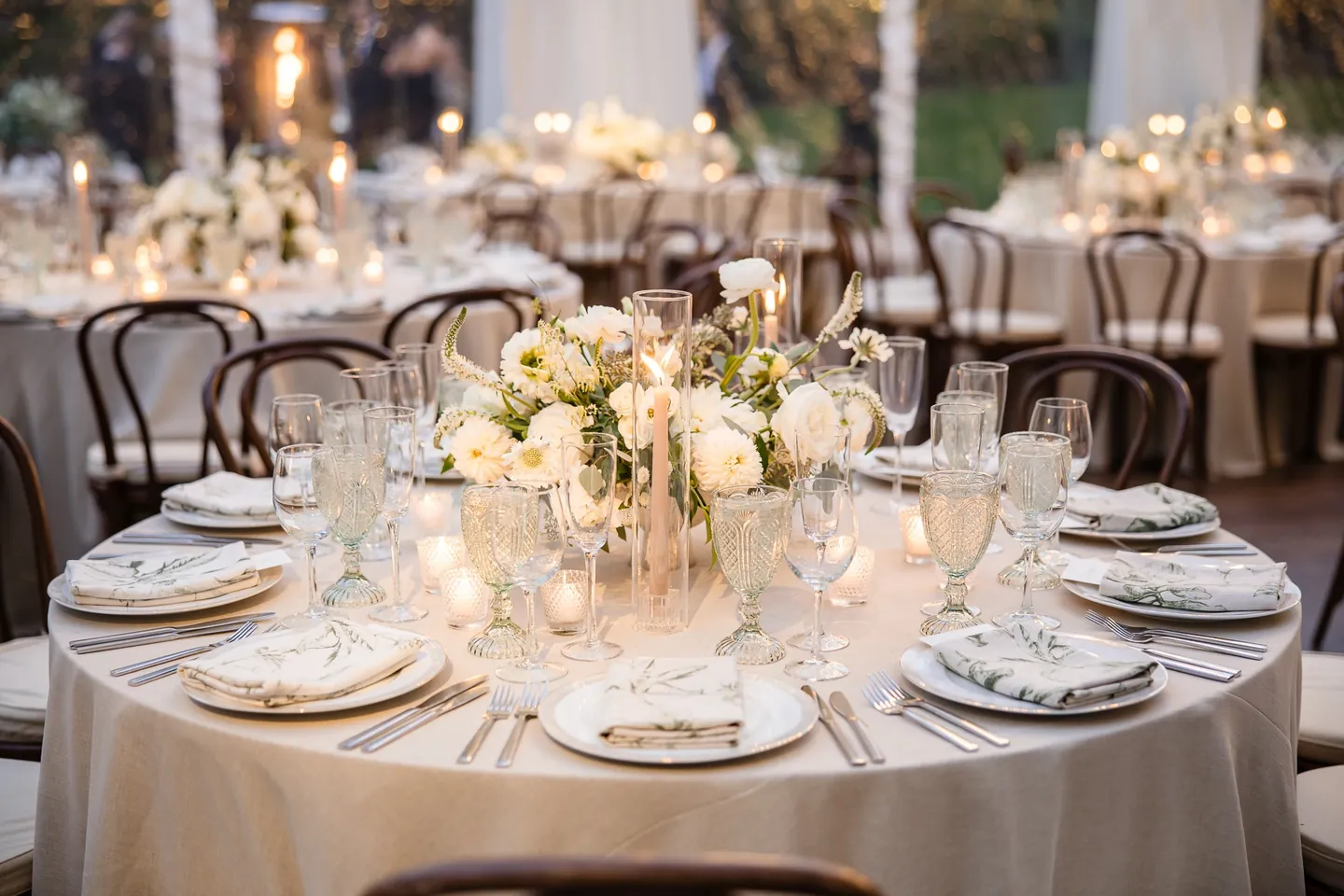 A round table set with white roses, candles, and gold-rimmed glassware