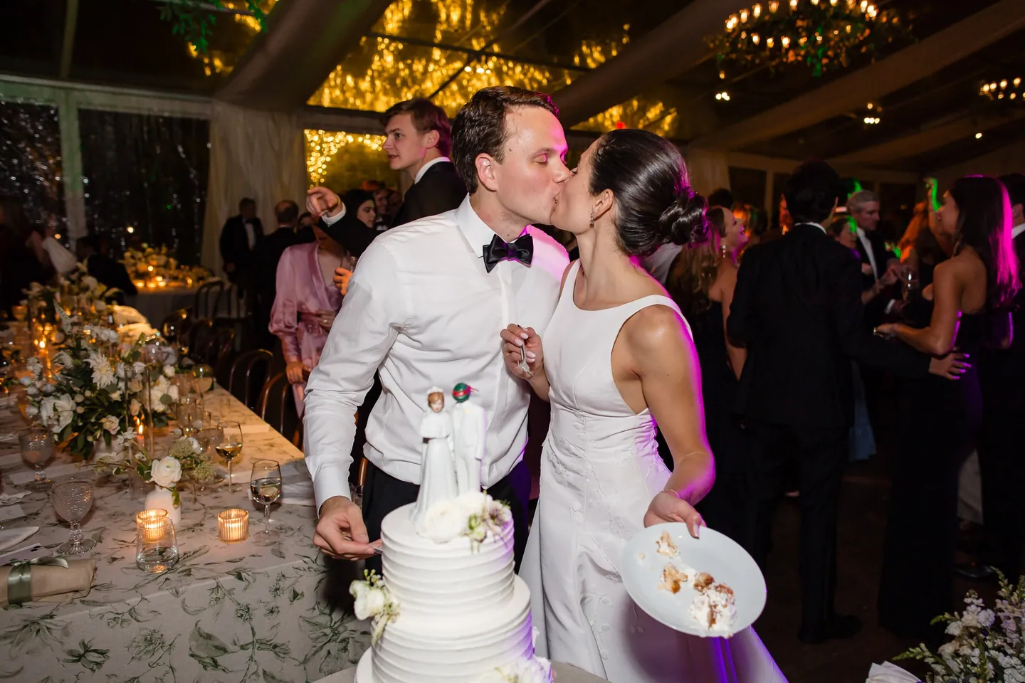 Angie and Matt kiss beside the cake as candles glow on the tables nearby