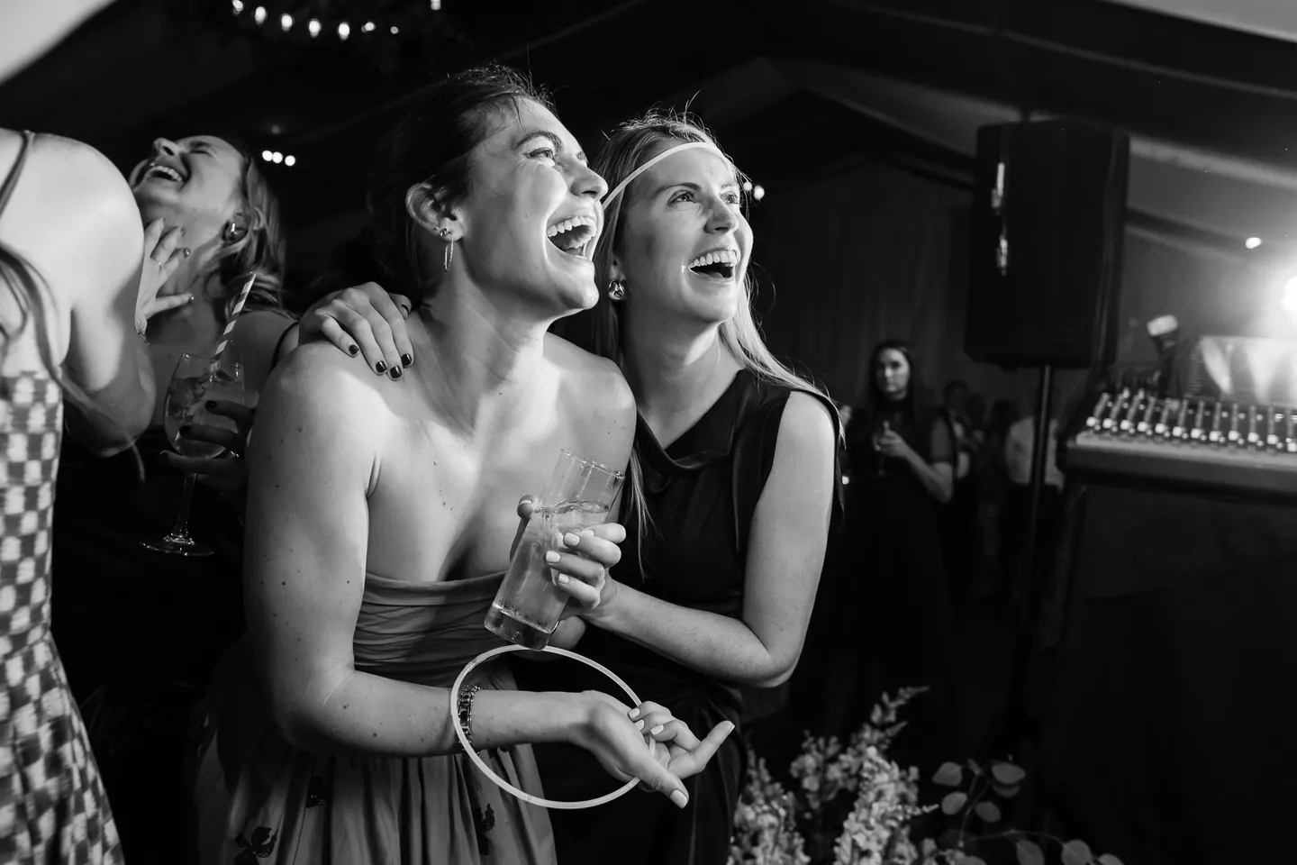 A pair of guests throw their heads back laughing near the band, in black and white