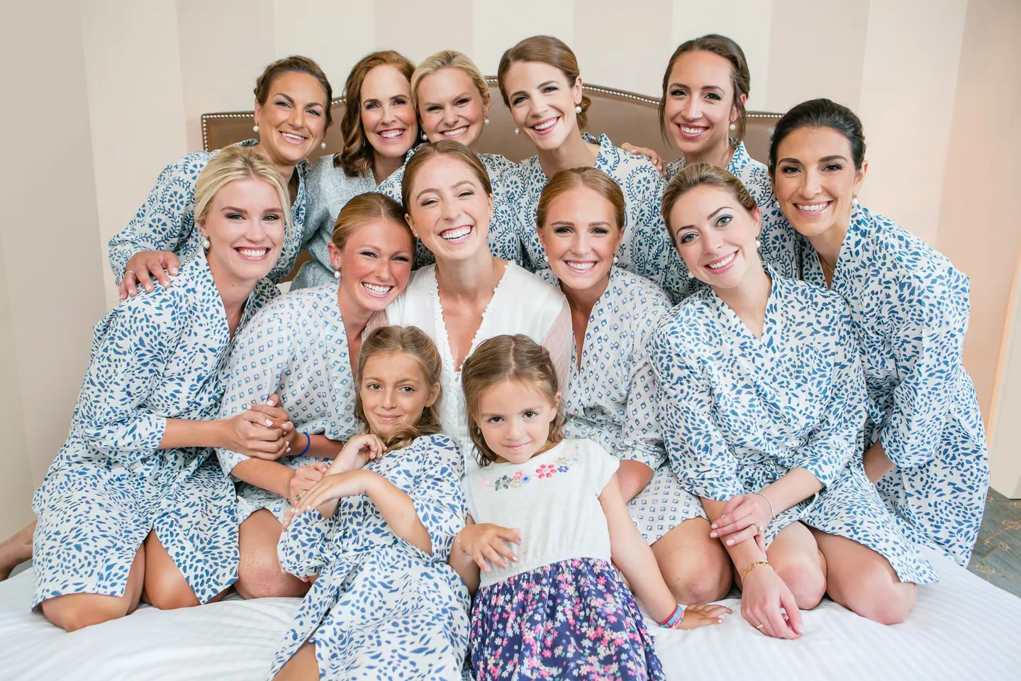 Bridesmaids in matching blue floral robes crowd around the bride and a flower girl