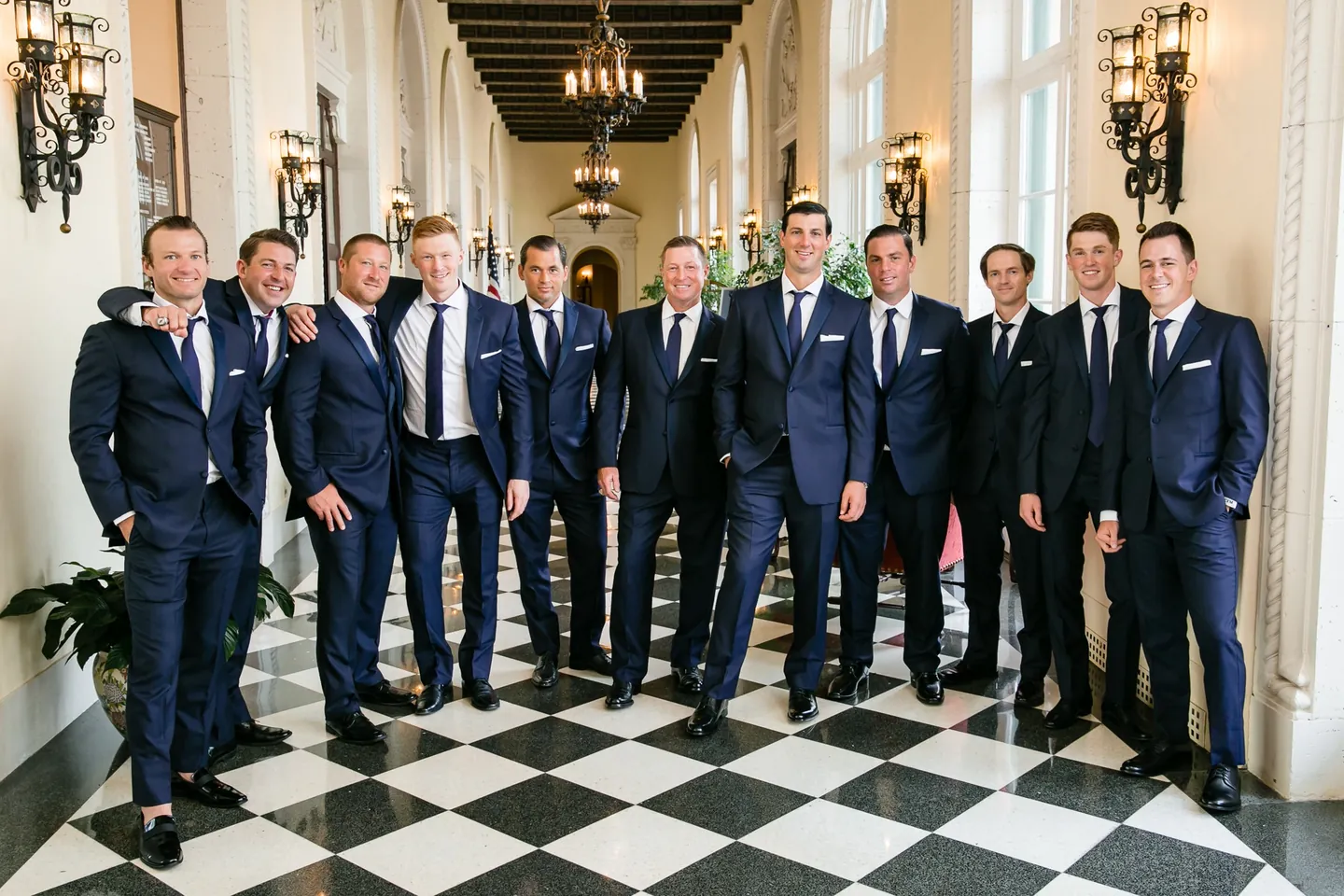 The groom and groomsmen in navy suits stand on a checkered marble floor