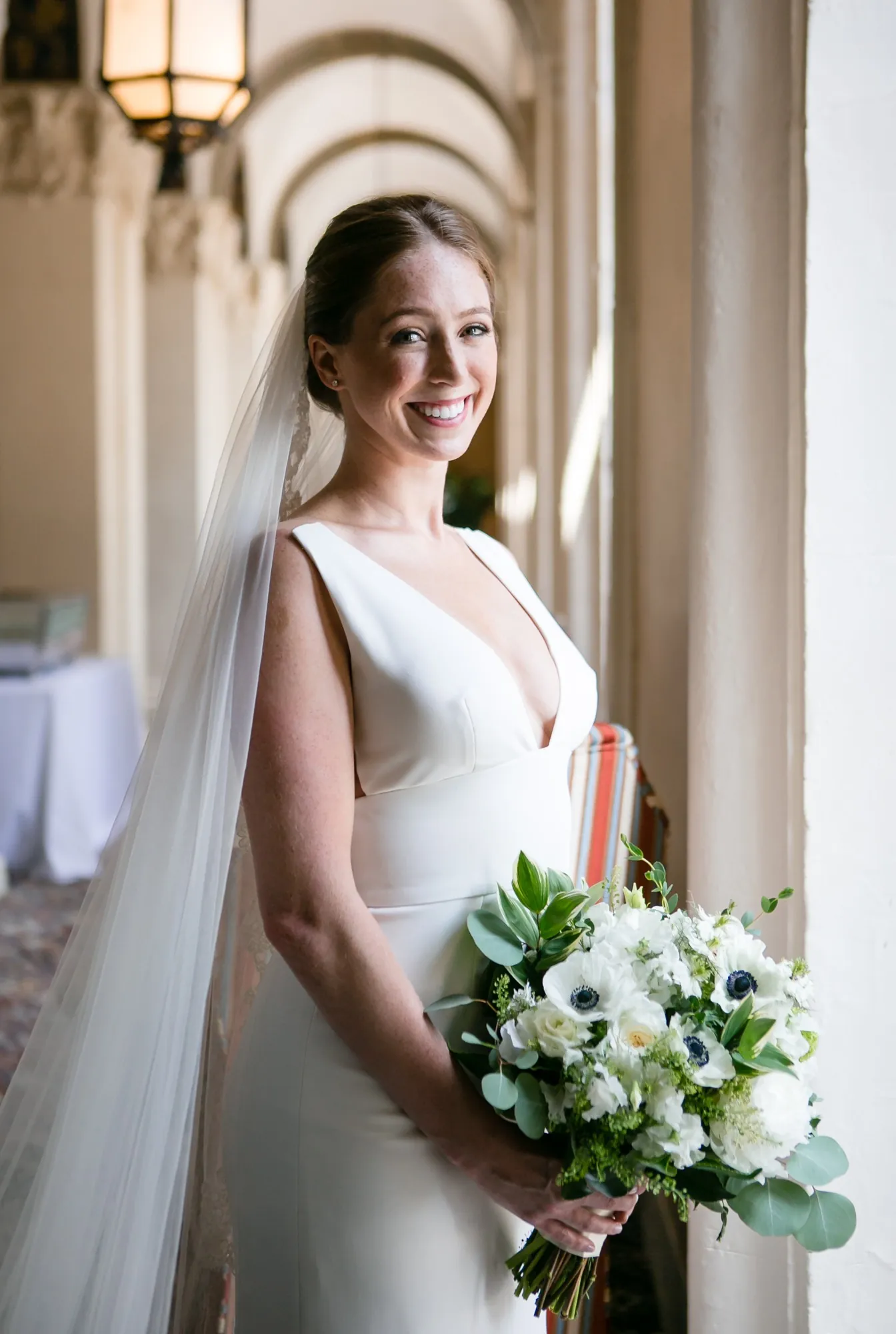The bride holds her bouquet under the arches of a long sunlit corridor