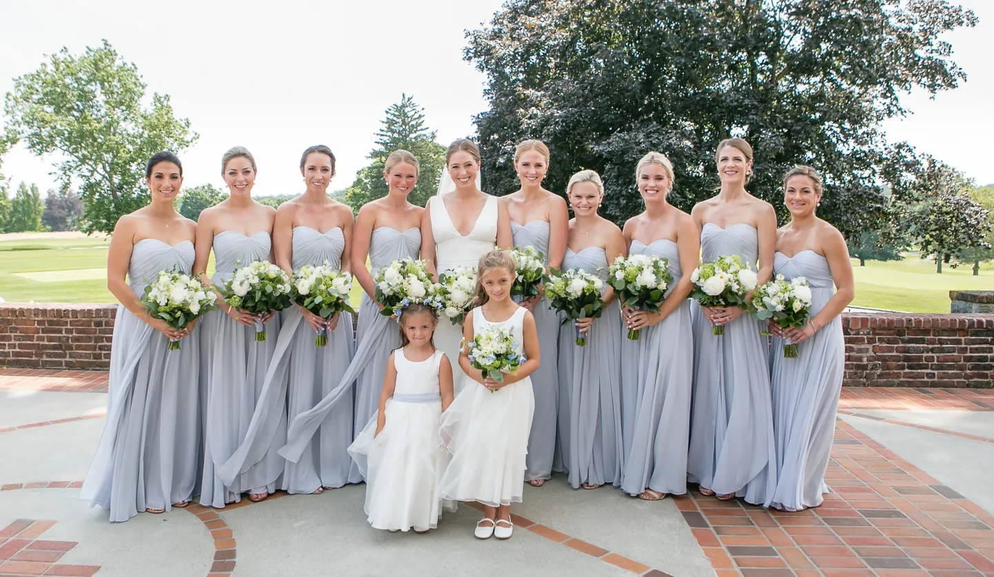 Bridesmaids in pale blue gowns and 2 flower girls pose on a brick terrace